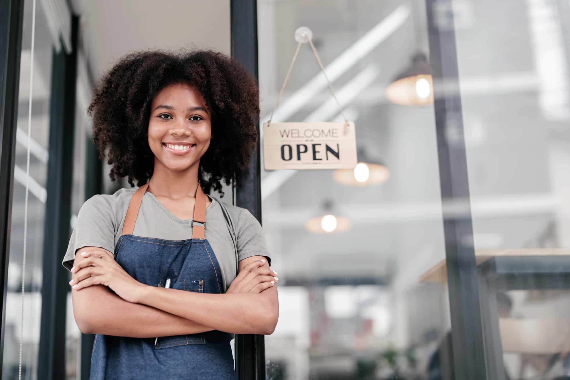 Smiling African American barista with apron standing welcomingly at a cafe door